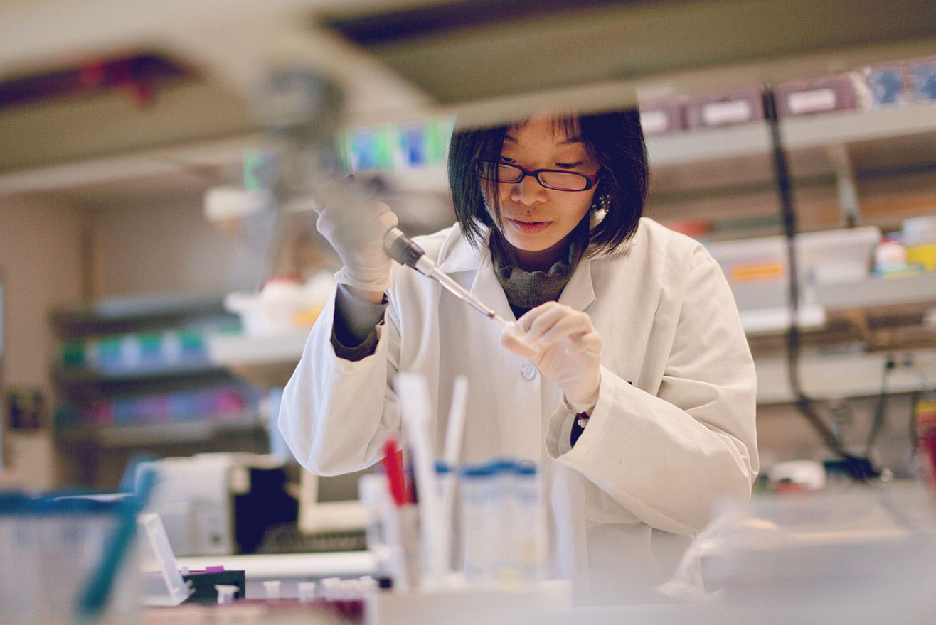 A laboratory technician in a white coat uses a pipette, in a laboratory.