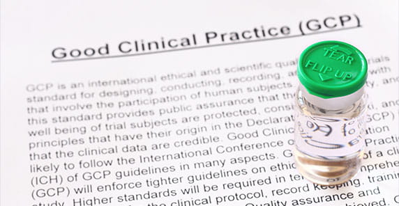 A vial with a green cap labeled "Tear Flip Up" sits beside a document titled "Good Clinical Practice (GCP)."