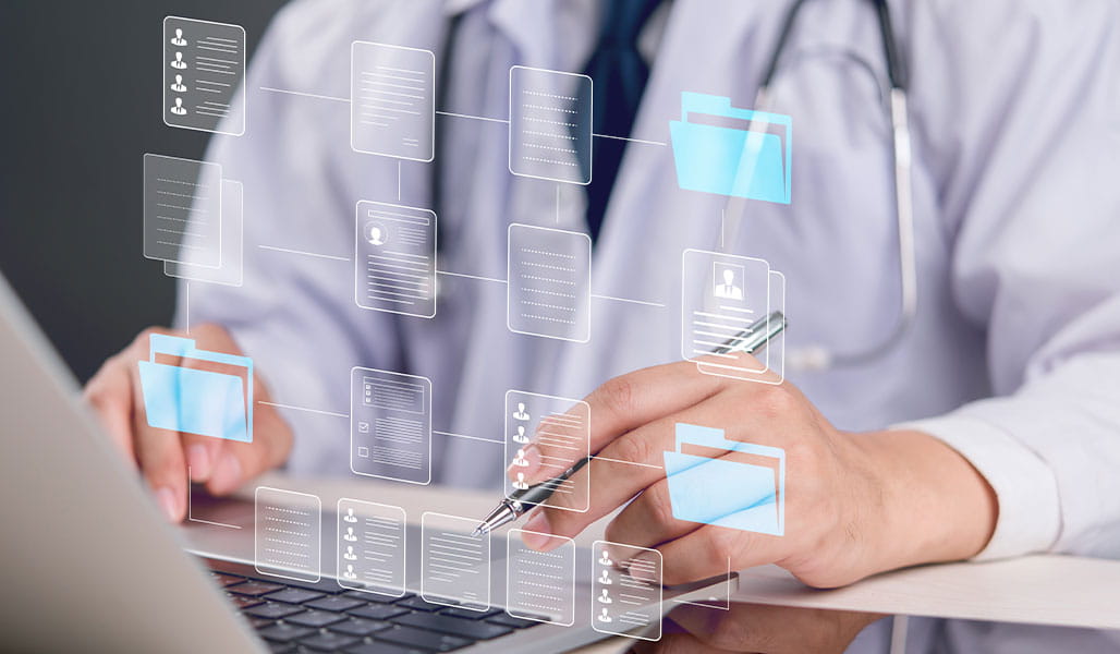 A healthcare professional in a white coat uses a laptop surrounded by digital icons representing patient records and data.