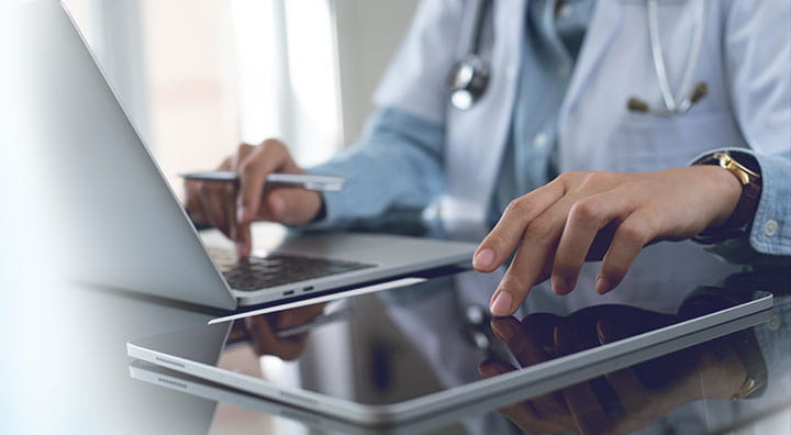 Doctor using digital tablet and working on laptop computer at doctor's office in hospital