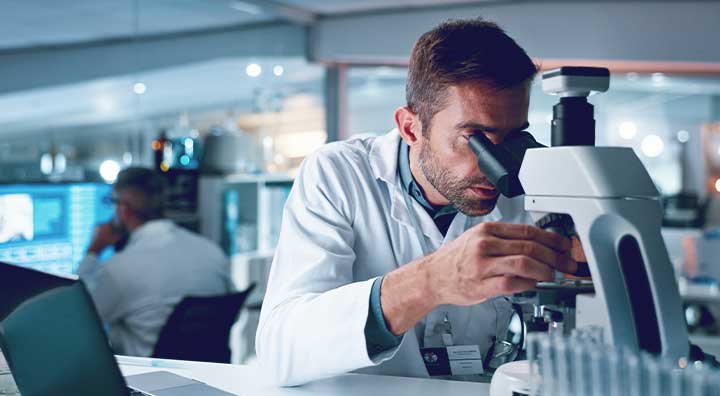 A male scientist in lab coat looking through a microscope.