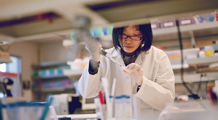 A scientist in a lab coat conducts an experiment, focused on using a pipette among various lab equipment and supplies.