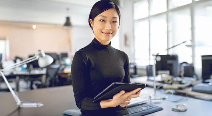 A person holds a tablet, standing in a modern office.